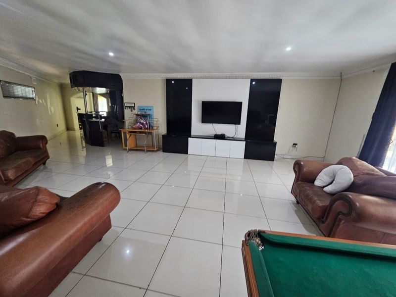 Spacious living room featuring large format floor tiles, a modern built-in media wall, and a dedicated bar area with recessed lighting.