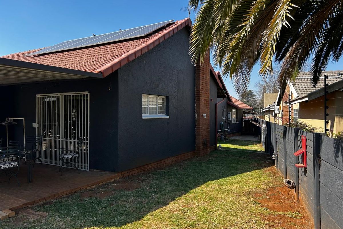 Rear view of the property featuring a covered patio, tiled roof with solar panels, brick chimney, and a fenced garden area.