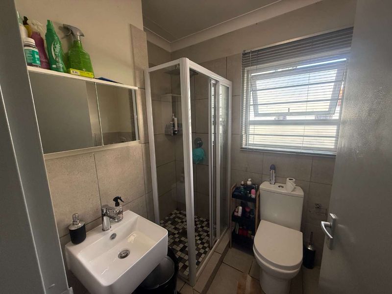 A functional bathroom featuring a shower enclosure, basin with vanity mirror, and toilet, finished with neutral wall and floor tiles.