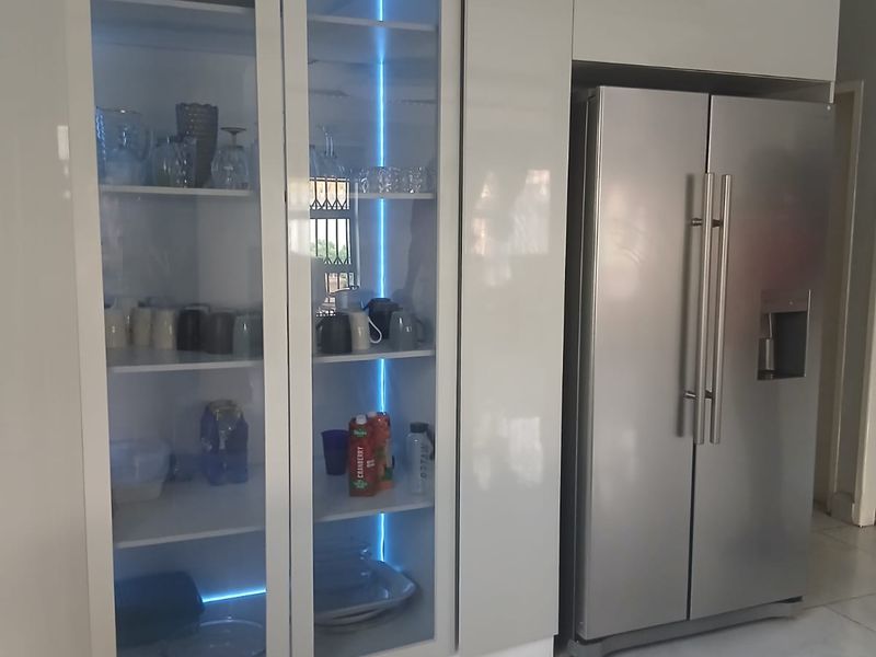 Modern kitchen featuring high-gloss cabinetry with integrated glass-fronted display units and ambient LED lighting, complemented by sleek tiled flooring.