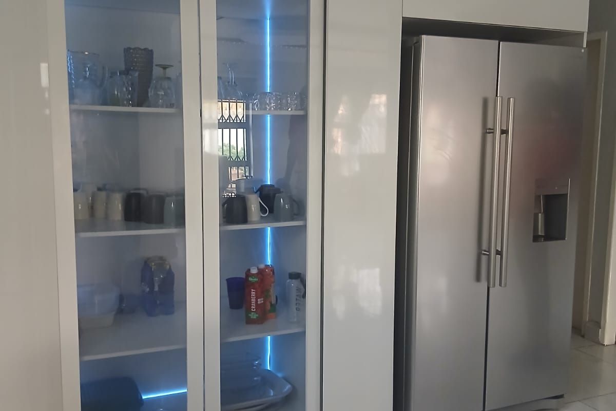 Modern kitchen featuring high-gloss cabinetry with integrated glass-fronted display units and ambient LED lighting, complemented by sleek tiled flooring.