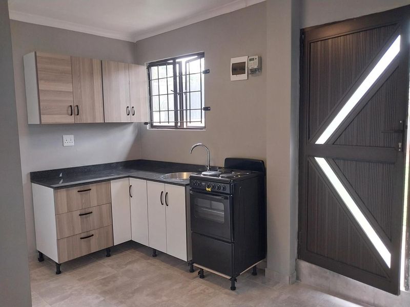 A clean, modern kitchen featuring light wood-tone cabinetry, dark countertops, a freestanding stove, and tiled flooring with secure window bars.