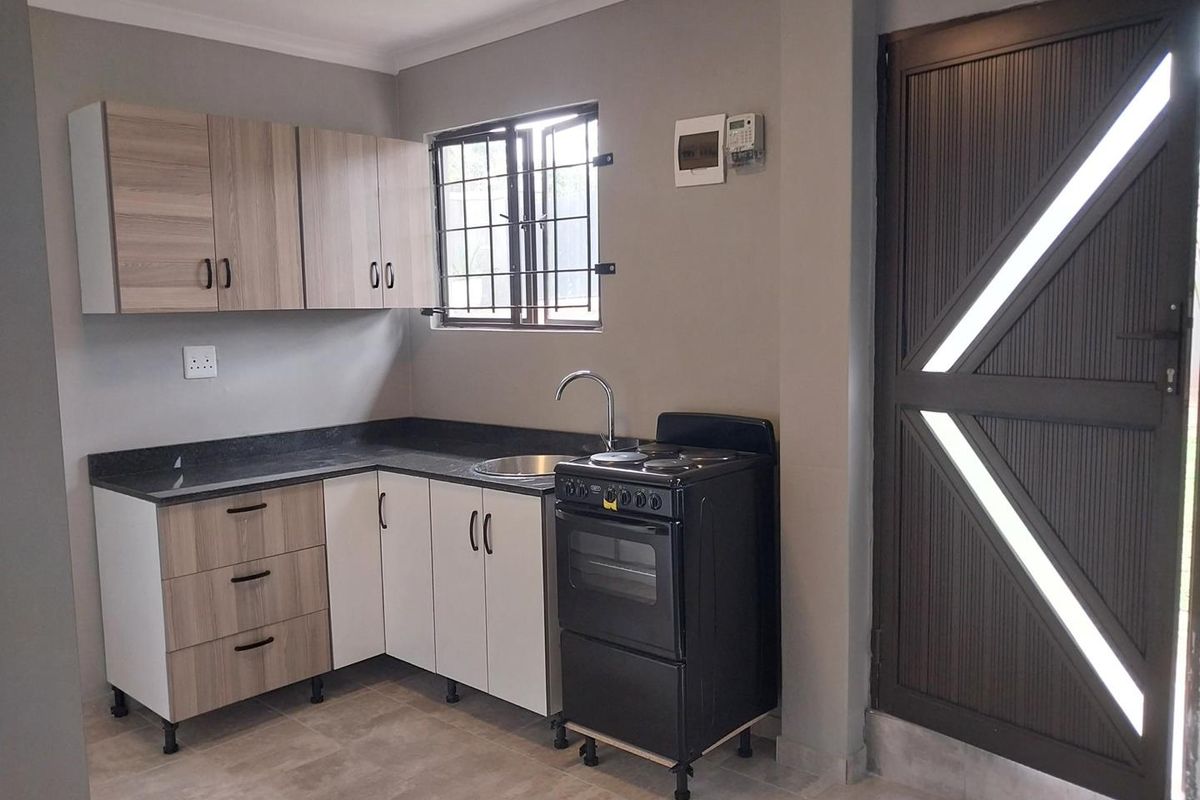 A clean, modern kitchen featuring light wood-tone cabinetry, dark countertops, a freestanding stove, and tiled flooring with secure window bars.
