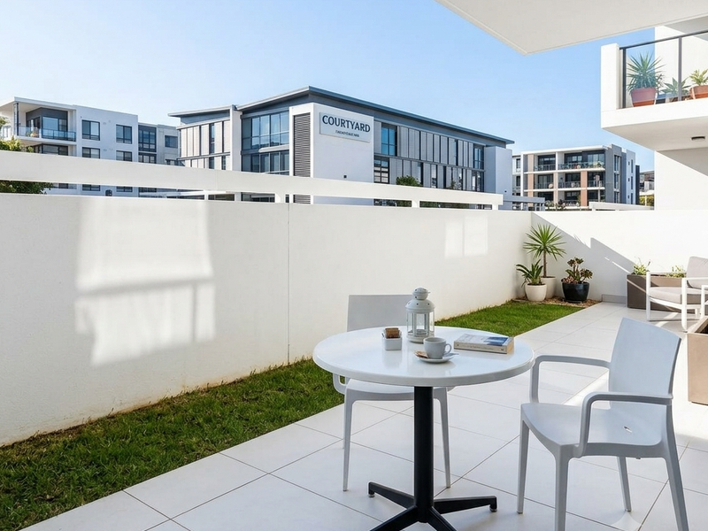 A modern, well-maintained ground-floor balcony featuring large format floor tiles, a clean white railing, and a small integrated garden area.