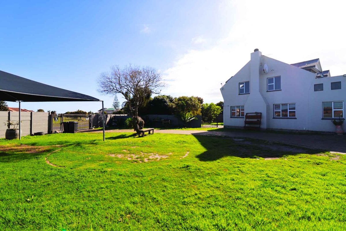 Rear view of the property featuring a spacious lawn, paved driveway, perimeter walling, and a shade sail structure.
