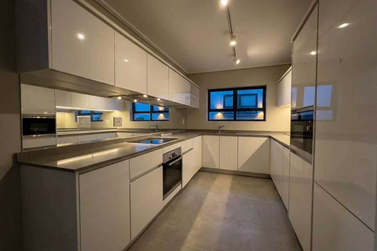 Modern, sleek kitchen featuring high-gloss cabinetry, integrated appliances, stone countertops, and a mirrored splashback, offering a clean and contemporary aesthetic.