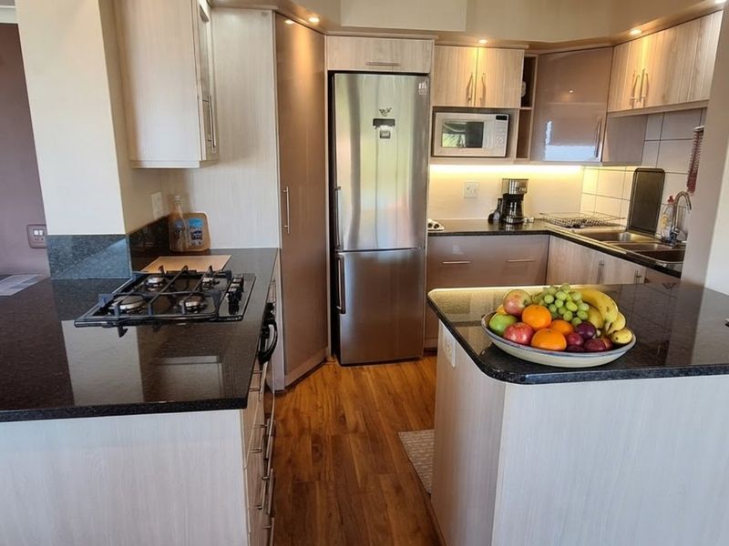 A functional kitchen featuring granite countertops, light wood-finish cabinetry, a gas hob, and integrated appliances with warm under-cabinet lighting.