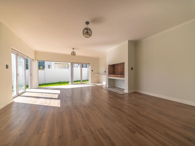 Spacious open-plan living area featuring modern laminate flooring, built-in braai, and large sliding doors opening to the garden.