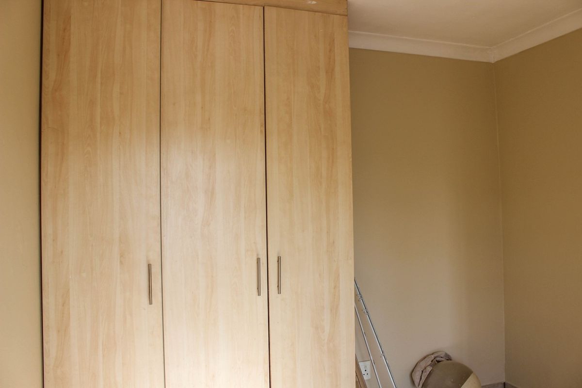 A bedroom interior featuring light wood-finish built-in wardrobes and neutral wall paint with decorative coving.