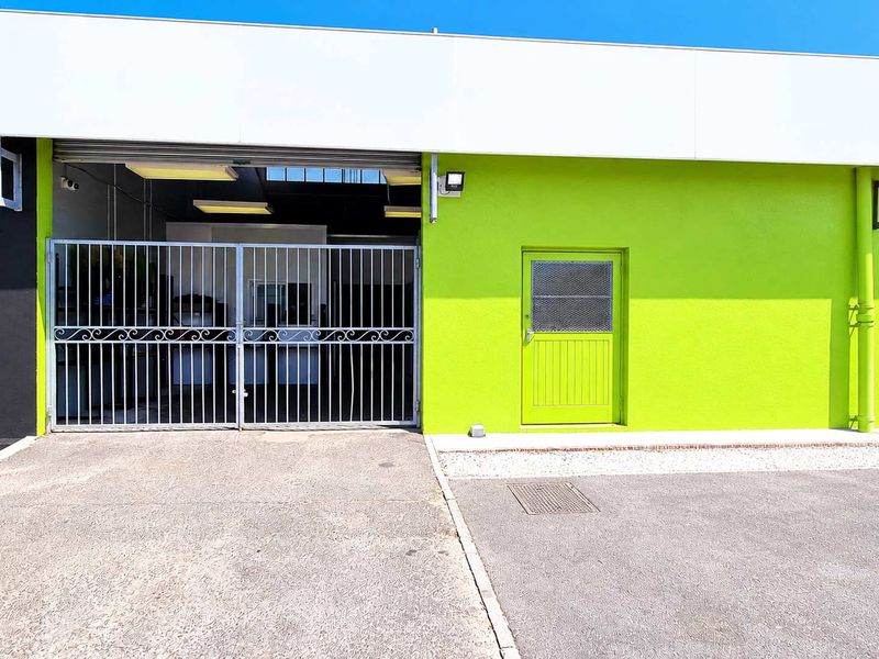 Front facade of an industrial unit featuring a roller shutter door, security gate, and a bright green painted exterior wall.