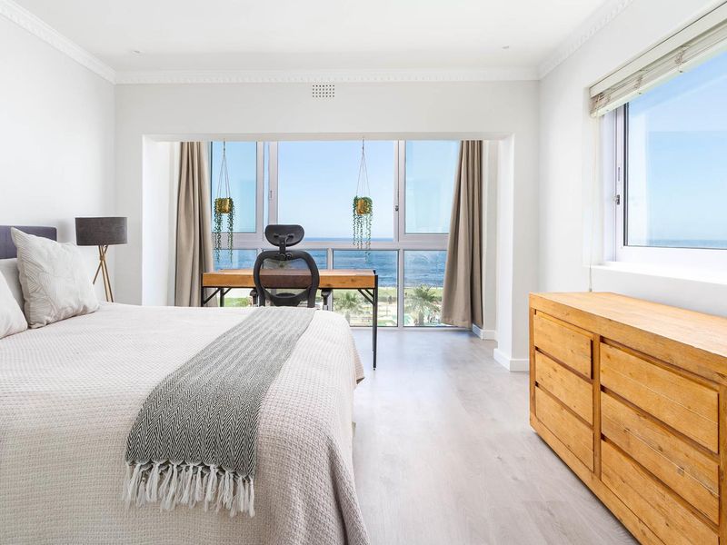 A bright and spacious bedroom featuring large windows with expansive ocean views, modern laminate flooring, and elegant crown molding.