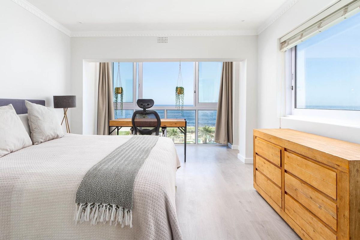 A bright and spacious bedroom featuring large windows with expansive ocean views, modern laminate flooring, and elegant crown molding.