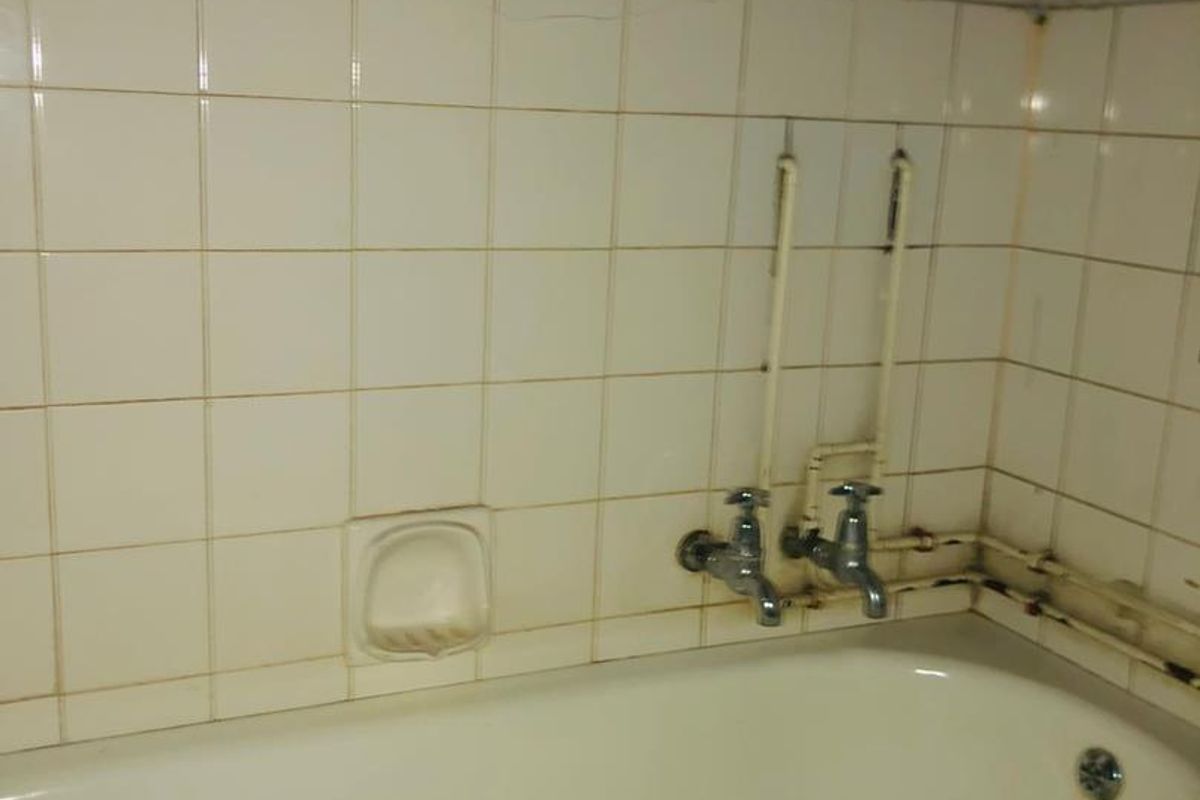 A dated bathroom featuring a standard bathtub with exposed plumbing and ceramic wall tiling, requiring renovation to address wear and finish deterioration.