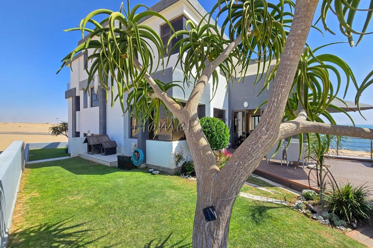 A view of the rear exterior of the house featuring a landscaped garden, a wooden deck, and modern architectural finishes.