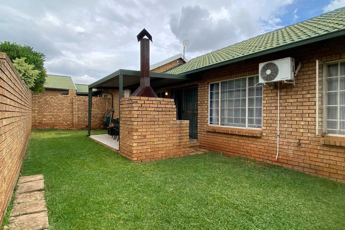 Rear exterior view of the townhouse featuring a private garden, a covered patio area with a built-in brick braai, and an external air conditioning unit.