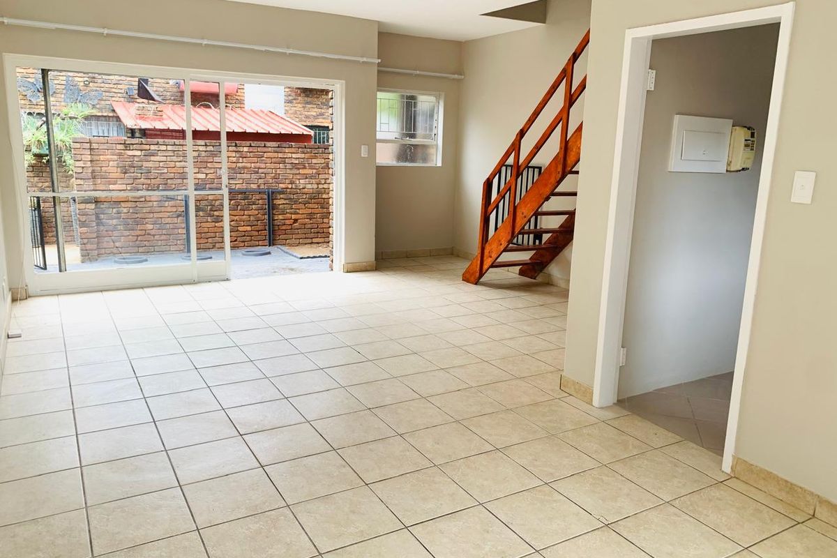 An open-plan living area featuring ceramic floor tiles, a wooden staircase, and a sliding glass door providing access to an outdoor patio area.