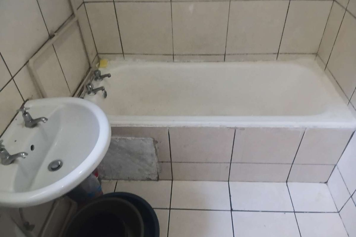 A dated bathroom featuring a standard bathtub and pedestal basin with ceramic tiling throughout, requiring cosmetic updates to improve its overall condition.