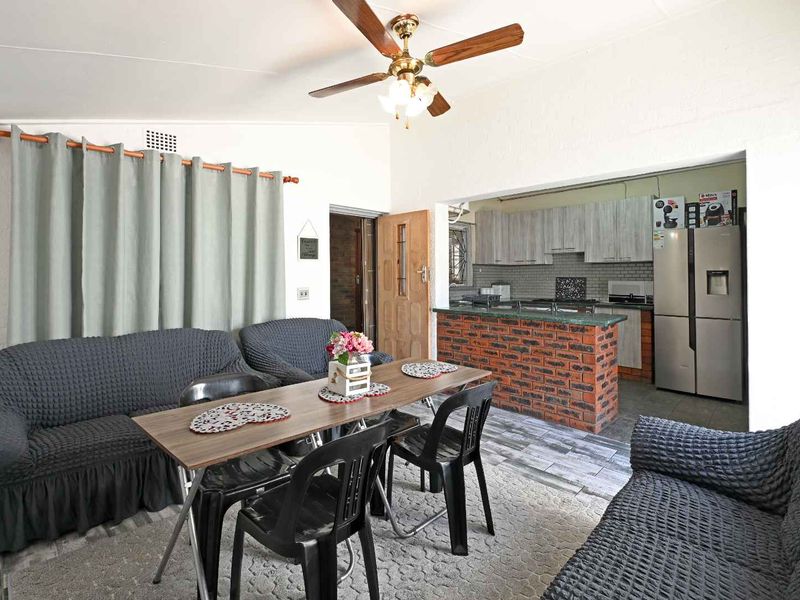 Open plan living and dining area featuring a kitchen with exposed brick breakfast bar, modern cabinetry, and tiled flooring throughout.