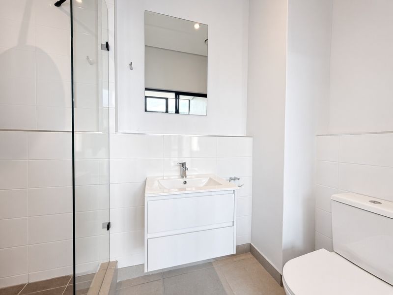 A clean, modern bathroom featuring a wall-mounted vanity, glass shower enclosure, and neutral ceramic tiling throughout.