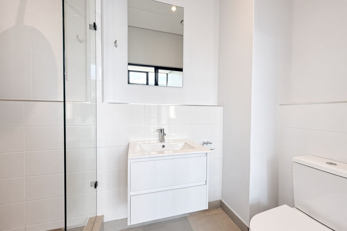 A clean, modern bathroom featuring a wall-mounted vanity, glass shower enclosure, and neutral ceramic tiling throughout.
