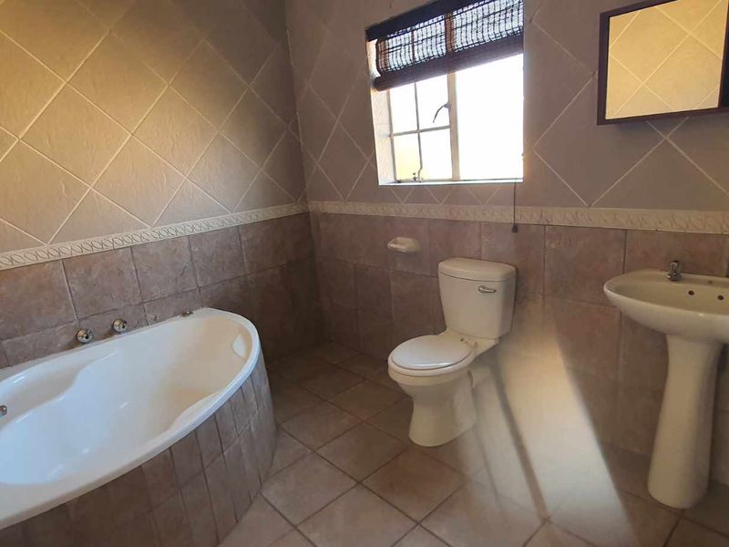 A functional bathroom featuring a built-in bathtub, pedestal basin, and toilet with neutral wall and floor tiling.