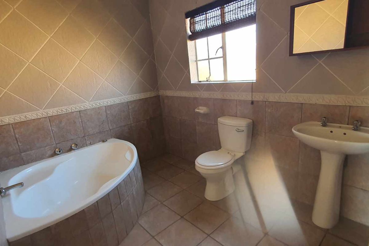 A functional bathroom featuring a built-in bathtub, pedestal basin, and toilet with neutral wall and floor tiling.