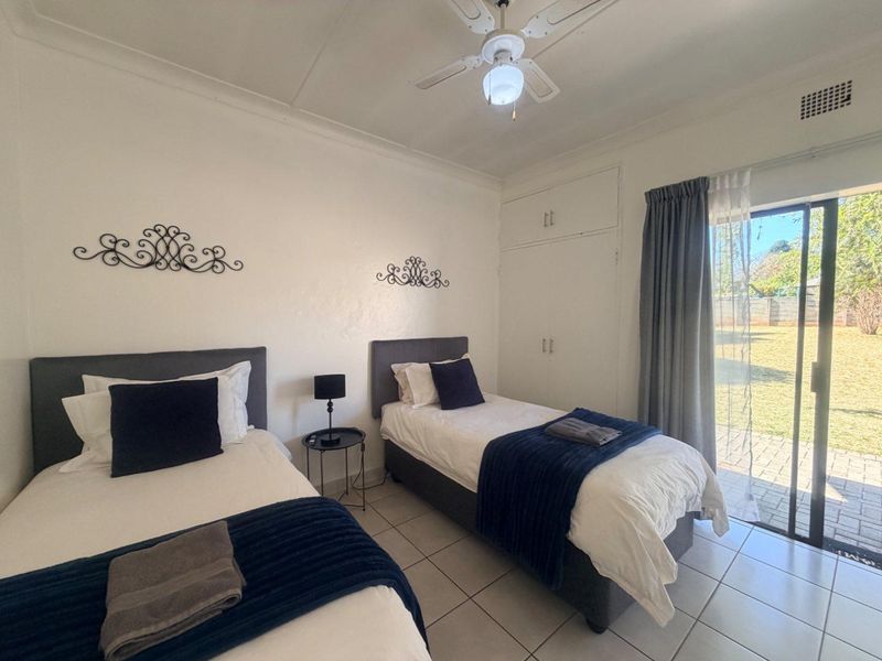 A bedroom featuring tiled flooring, built-in cupboards, a ceiling fan, and a sliding glass door providing direct access to the rear garden.