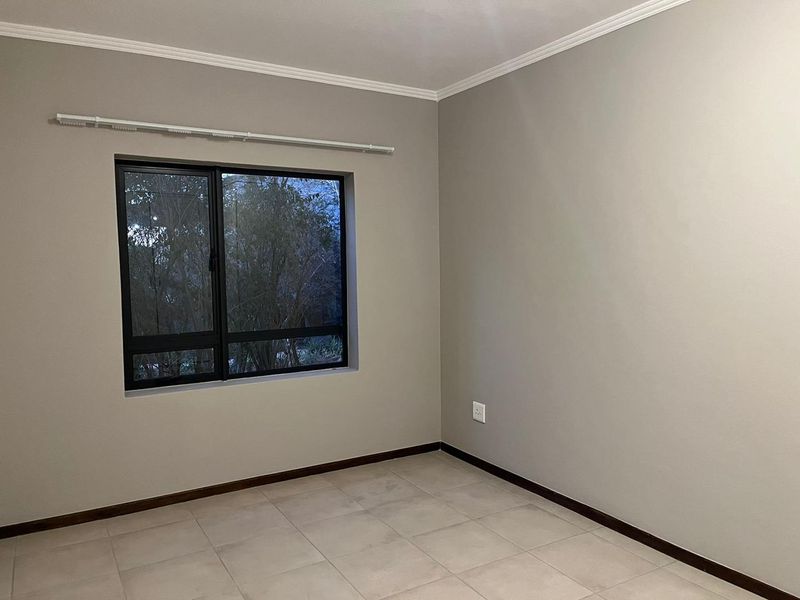 A clean, empty bedroom featuring neutral wall paint, tiled flooring, and a large aluminium-framed window with an installed curtain rail.