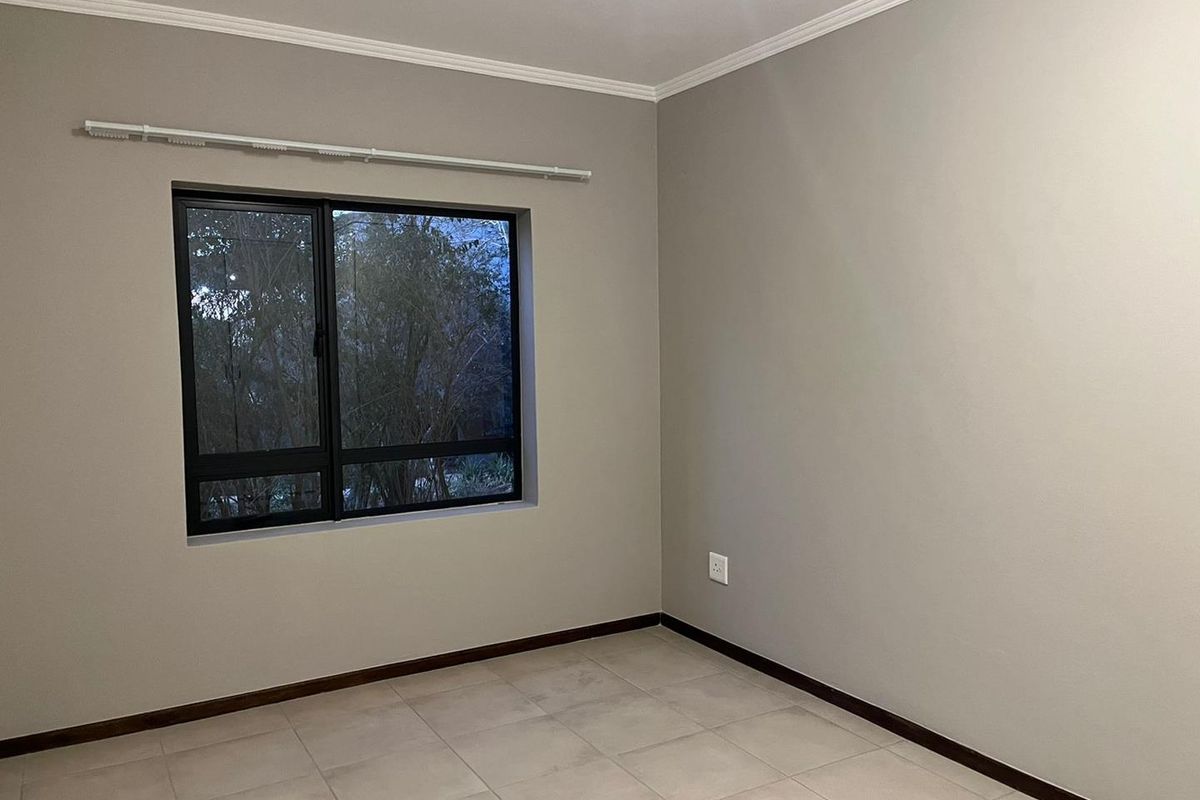 A clean, empty bedroom featuring neutral wall paint, tiled flooring, and a large aluminium-framed window with an installed curtain rail.