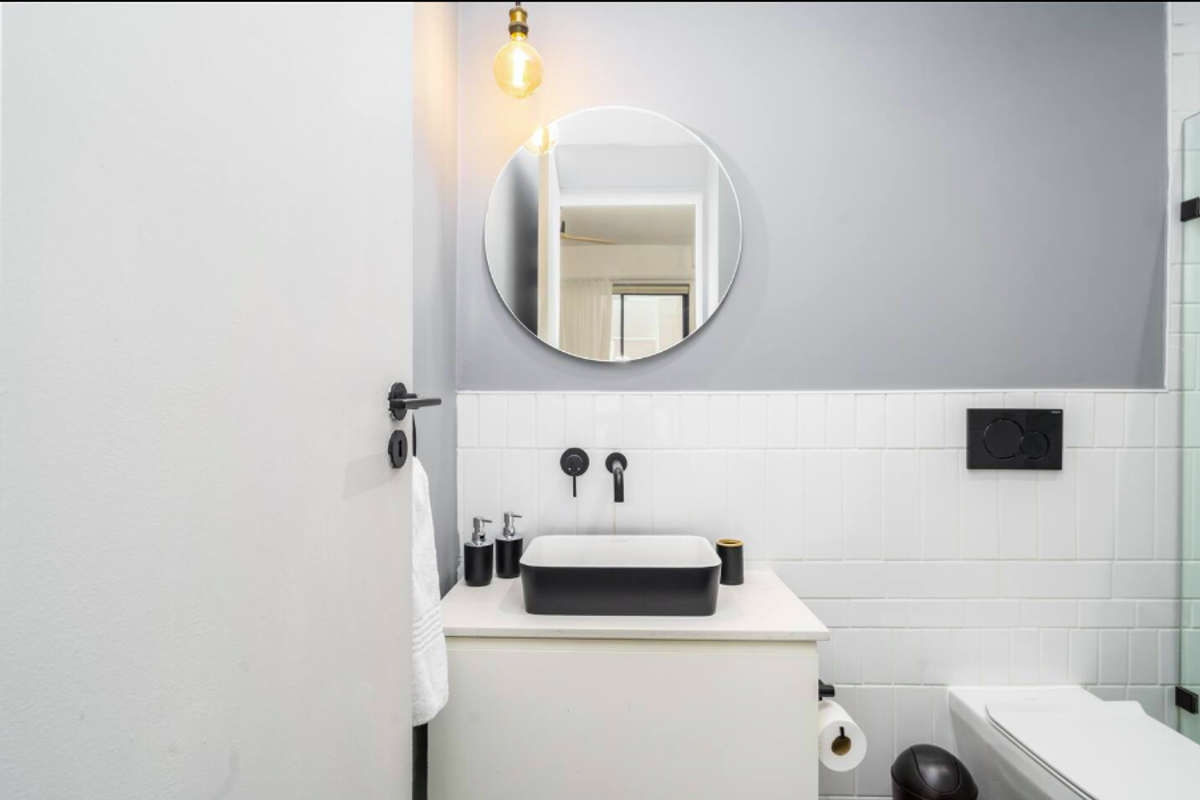 Modern bathroom featuring a contemporary vessel sink, wall-mounted matte black faucet, circular mirror, and white subway tile backsplash.