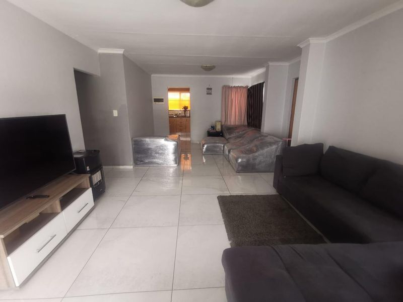 Open plan living area featuring large format porcelain floor tiles and neutral wall finishes, with a direct view through to the kitchen area.