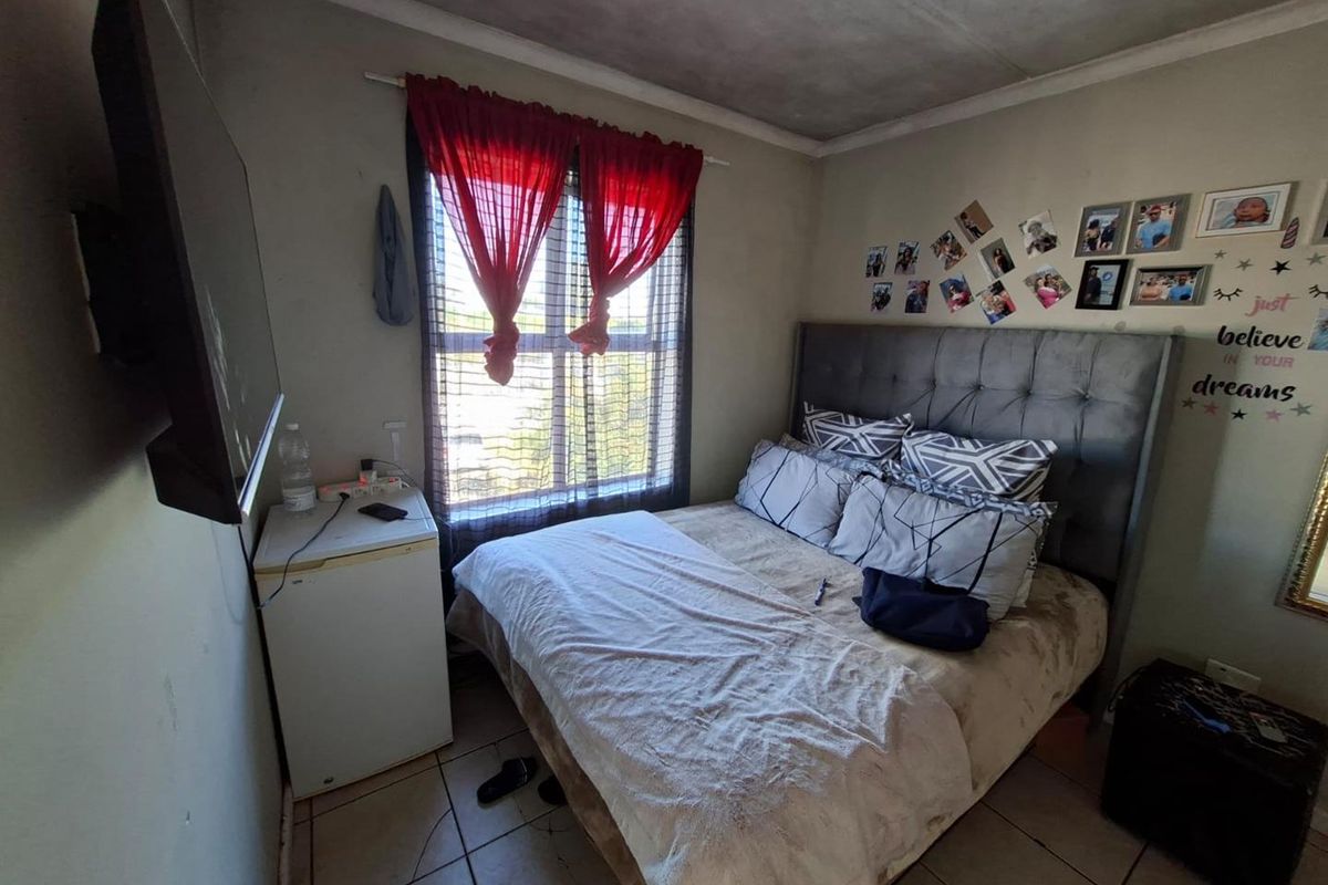 A compact bedroom featuring tiled flooring and a window, currently showing signs of wear on the ceiling and walls.