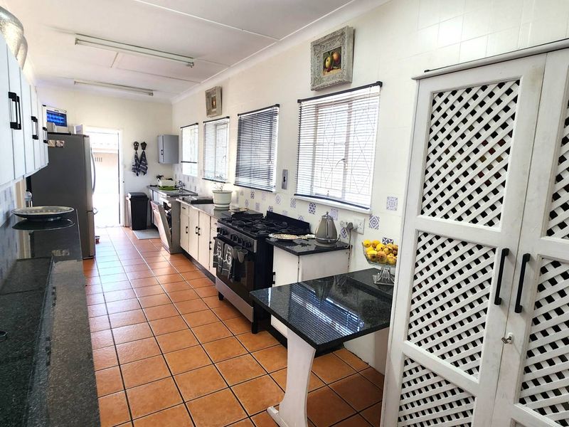 A functional kitchen featuring granite countertops, a gas stove, tiled flooring, and ample built-in cabinetry with a distinct lattice-style pantry door.