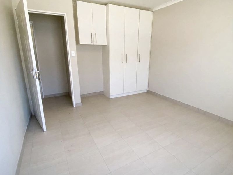 A clean, empty bedroom featuring neutral tiled flooring, built-in white cupboards, and simple cove cornice detailing.