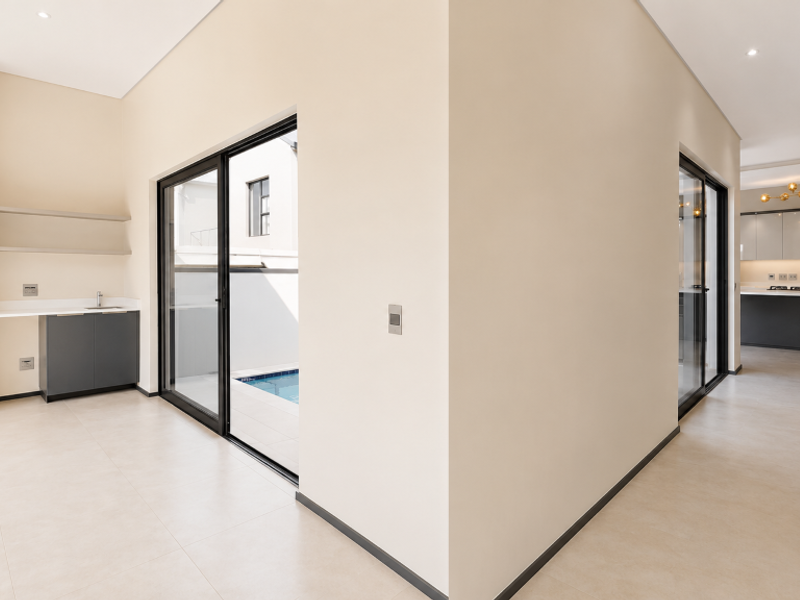 Modern open-plan living area featuring a built-in braai, sleek kitchen cabinetry, and seamless access to the outdoor pool area through sliding glass doors.