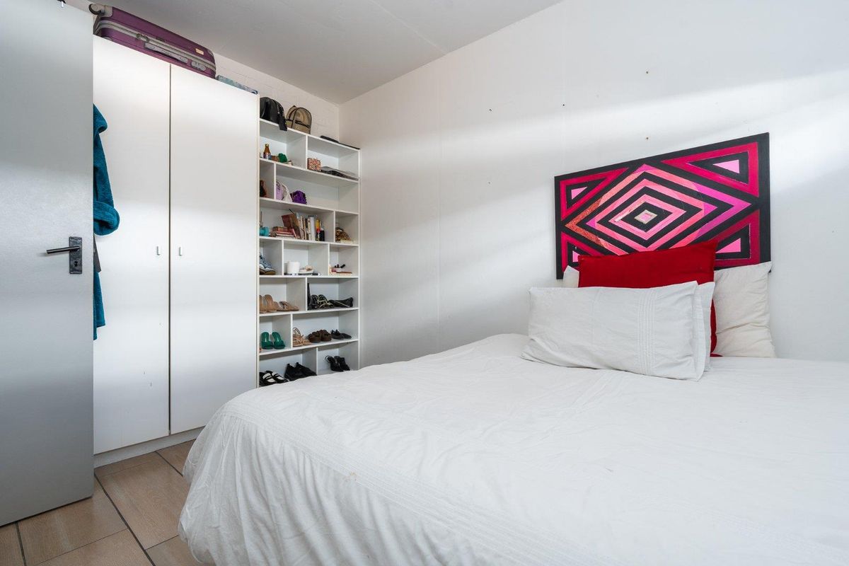 A functional bedroom featuring built-in wardrobe storage and integrated shelving, finished with tiled flooring.