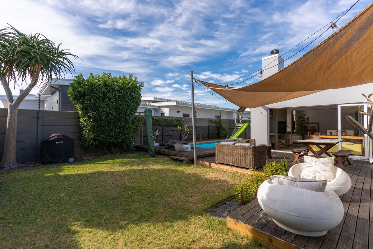 A well-maintained rear garden featuring a timber deck, swimming pool, outdoor fireplace, and shade sail, perfect for outdoor entertaining.