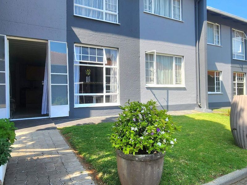 Front exterior view of a townhouse unit featuring a paved walkway, manicured lawn, and multi-pane windows with a direct entrance.