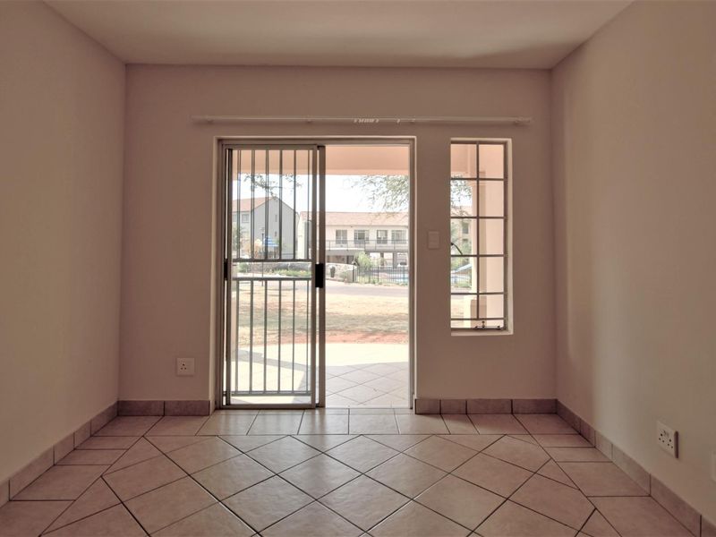 An empty living area featuring tiled flooring, a sliding glass door with a security gate, and a fixed window providing natural light.