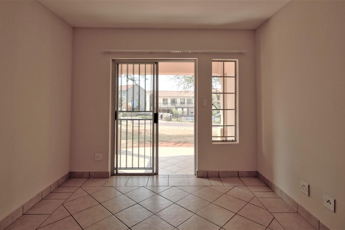 An empty living area featuring tiled flooring, a sliding glass door with a security gate, and a fixed window providing natural light.
