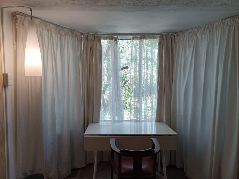 A bedroom area featuring a large window with floor-to-ceiling curtains and a pendant light fixture.