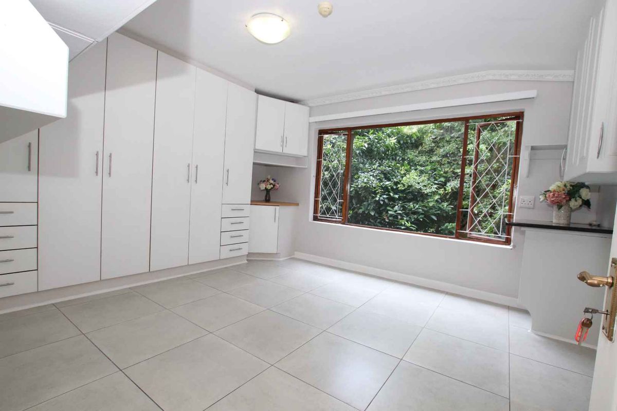 A bright bedroom featuring extensive built-in white cabinetry, large windows with security bars, and neutral floor tiling.