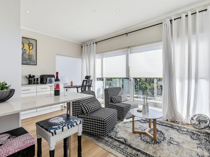 A bright open-plan living and kitchen area featuring modern cabinetry, stone countertops, laminate flooring, and large sliding doors leading to a balcony.
