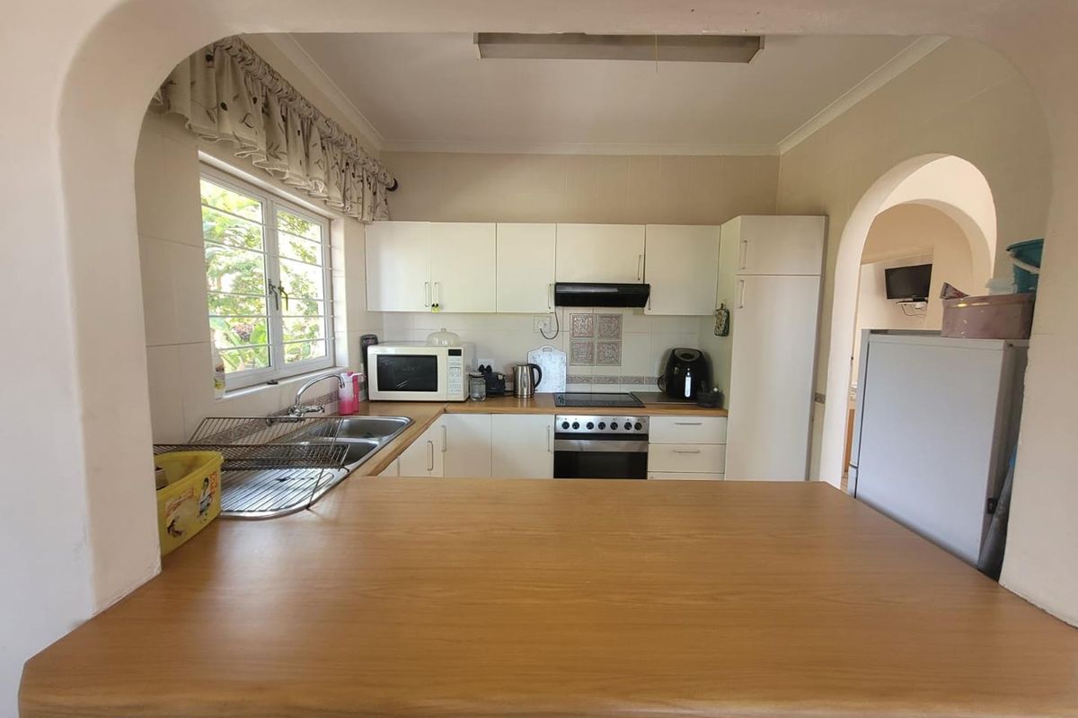 A functional kitchen featuring white cabinetry, a built-in oven with extractor fan, double sink, and a wooden breakfast bar counter.