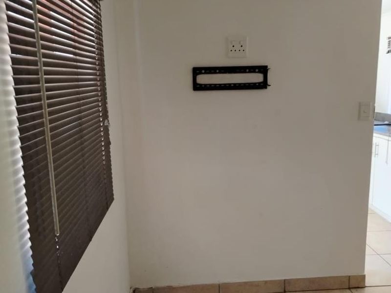 An empty living area featuring ceramic floor tiles, venetian blinds, and a wall-mounted TV bracket, providing a neutral space ready for personalization.