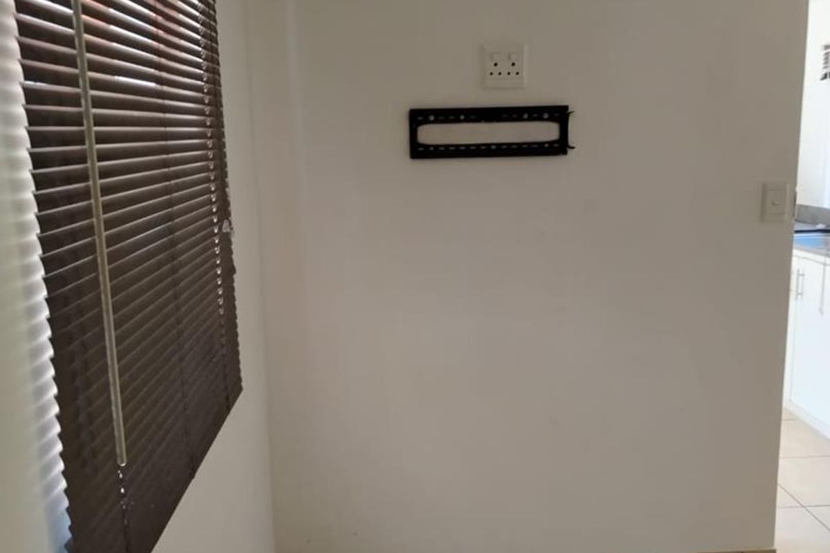An empty living area featuring ceramic floor tiles, venetian blinds, and a wall-mounted TV bracket, providing a neutral space ready for personalization.