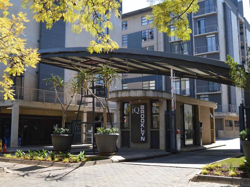 The entrance to iQ Brooklyn apartment complex featuring a modern security gatehouse, boom gate access, and contemporary multi-story residential architecture.