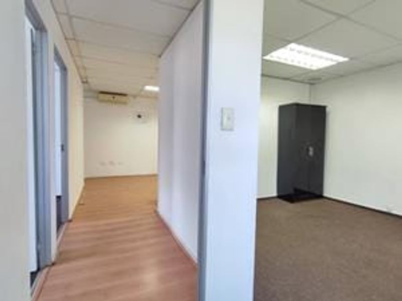 An empty office space featuring a mix of laminate and carpet flooring, suspended ceilings with recessed lighting, and an integrated air conditioning unit.