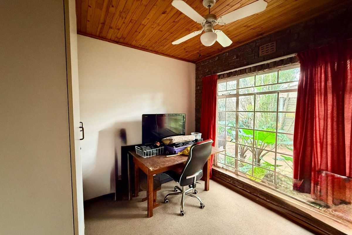 A bedroom featuring a timber-clad ceiling, ceiling fan, and large window with security bars, overlooking the garden area.