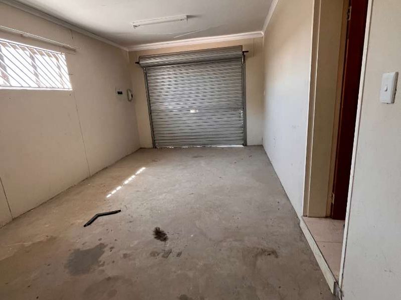 A vacant garage space featuring a roller shutter door, concrete flooring, and security-barred windows, offering potential for storage or workshop conversion.
